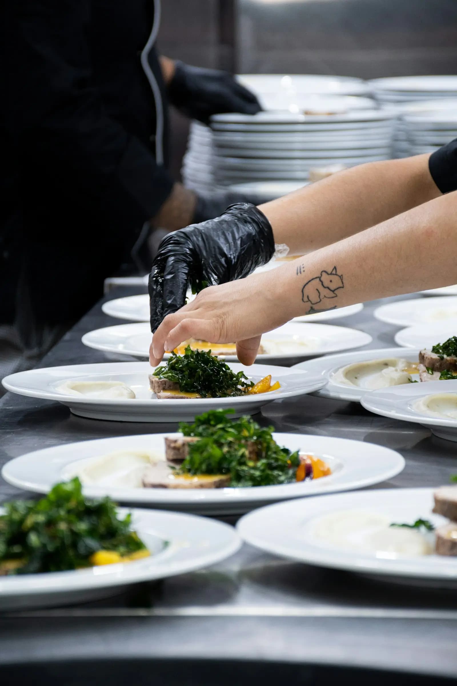 Una cocinera emplata en el pase una fila de platos iguales antes de que salgan a sala